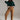 Full body look of caramel relaxed fit cotton trousers styled with green sweater, white sneakers, and cap for casual chic outfit