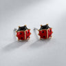 Catarina Stud Earrings featuring glossy red enamel ladybug design with black spots and gold detailing, displayed as a pair on a soft light gray background with subtle shadow, small dainty everyday stud earrings