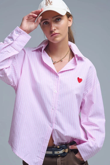 Pink and white striped button-down shirt with embroidered red heart detail on the chest, shown on model with relaxed fit — Cayana Shirt by Matte.
