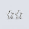Charleroi silver star hoop earrings with sculptural abstract silhouette, polished silver finish, and modern statement jewelry styling on a soft light gray background.
