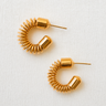 Gold coiled hoop earrings with sculptural spiral design displayed on light fabric background, Cicely Hoop Earrings by Matte.