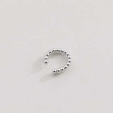 Claude Ear Cuff in polished silver featuring a rounded beaded open cuff design, styled as a sleek minimalist ear cuff on a soft neutral background.