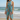 Model wearing turquoise sarong with coral tropical print tied as a beach wrap, standing by the ocean.
