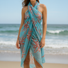 Model wearing turquoise sarong with coral tropical print tied as a beach wrap, standing by the ocean.
