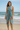 Model wearing turquoise sarong with coral tropical print tied as a beach wrap, standing by the ocean.
