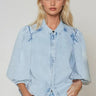 Model wearing the Corsica light-wash denim blouse with volume sleeves.
