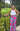 Woman in a white top and colorful pants standing outdoors with greenery around