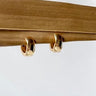 Gold Elena mini huggie earrings on a wooden surface