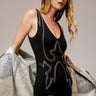 Woman wearing the Ephesus Bodysuit in black with bold metallic embroidery and a fitted V-neck silhouette, photographed in soft natural light on a neutral backdrop.