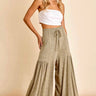 A female model wearing a white tube top and green wide leg pants with a high waist and tiered design.