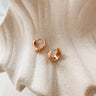 Faiza gold huggie earrings on a beige fabric background