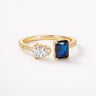Frills Ring gold open ring with pear cut clear crystal and deep blue emerald cut stone pavé band modern dual stone statement ring on neutral background.