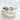 A silver-colored bracelet cuff with a cat design, featuring a central stone and surrounded by embellishments, displayed on a white cushion.