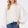 Model wearing the Giselle Blouse in white — semi-sheer, lightweight button-down with voluminous sleeves, styled with denim jeans against a neutral background, front close up.