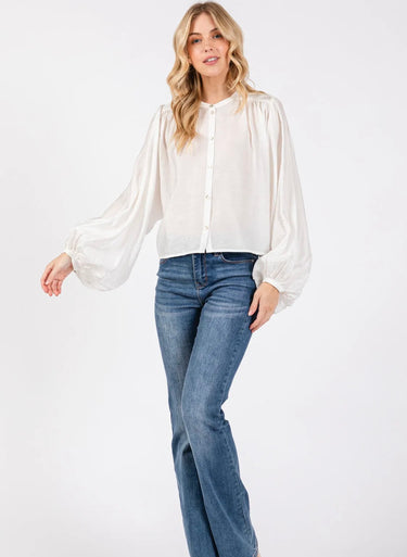 Model wearing the Giselle Blouse in white — semi-sheer, lightweight button-down with voluminous sleeves, styled with denim jeans against a neutral background.