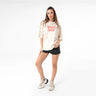 Happy Hour T-Shirt full outfit view showing oversized cream t-shirt, red graphic print on chest, loose short sleeve silhouette, styled with neutral sneakers, photographed on white studio background.