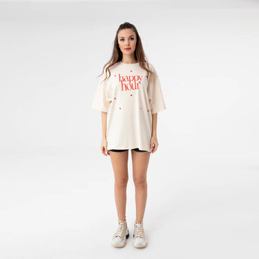 Happy Hour T-Shirt front-facing full body photo of model wearing oversized graphic tee with red lettering, relaxed loose fit falling mid-thigh, casual styling with sneakers, minimal clean studio background.