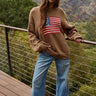 Woman wearing oversized knit sweater with American flag design, styled with jeans outdoors.