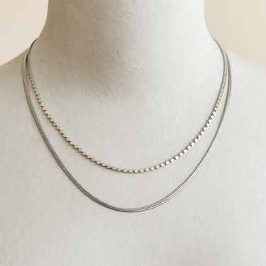 Silver double necklace on a mannequin with a plain background.