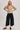 Model wearing High-Rise Pleated Culotte Pants in black, wide-leg cropped fit with pleated details and side pockets, styled with taupe sweater and loafers