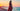 Woman in a red dress standing on a beach at sunset