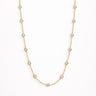 Iki Necklace gold zirconia version flat lay showing fine chain with small bezel-set clear stones on light neutral background with soft shadow.