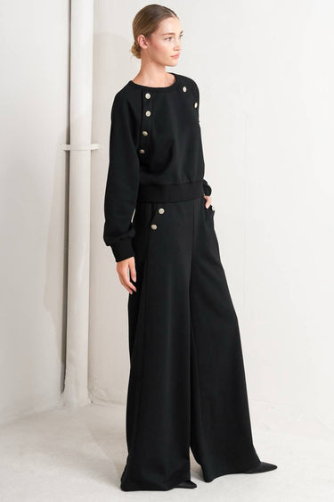 Woman wearing black pants with button details against a white background