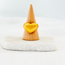A gold-filled heart-shaped ring displayed on a wooden stand against a white background.