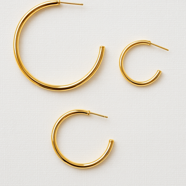 Isabel Hoop Earrings in gold finishes arranged on white fabric background in minimalist flat lay.