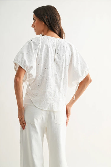 Woman wearing a white blouse with short sleeves and a V-neckline on a plain background