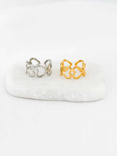 Gold-plated heart link rings displayed on a wooden stand with a white base.