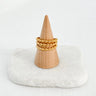 A gold-plated beaded ring displayed on a wooden stand with a white cushion
