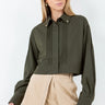 Woman wearing the Kairo Blouse in olive green, refined cropped silhouette with pintuck detailing and gold collar charms, photographed on a clean white background.