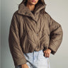 Model wearing the Karls Jacket in taupe, featuring diamond quilting, a padded stand collar, and snap-front closure, styled with light-wash jeans.