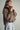 Side view of the Karls Jacket in taupe, showing diamond quilting, a padded stand collar, and relaxed sleeves, styled with light-wash jeans.