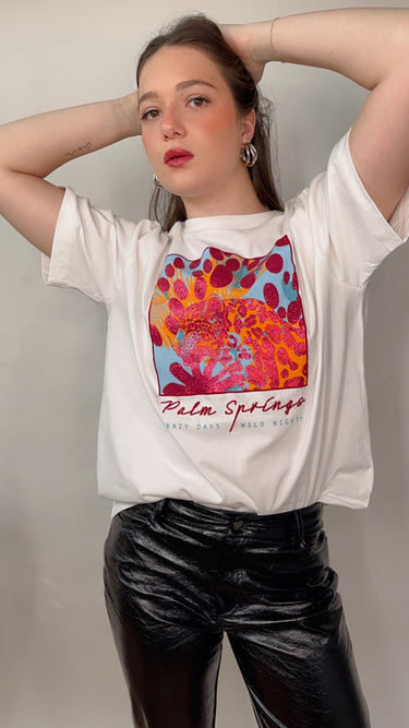 Model wearing the Katerina Tee — white cotton t-shirt with colorful Palm Springs graphic print, relaxed fit, short sleeves, modern casual style.