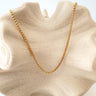 A gold-plated chain necklace displayed on a textured beige surface.
