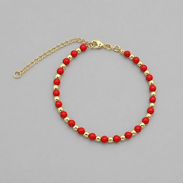 Kip Bracelet close-up of red beaded bracelet with gold accents on neutral background, highlighting color contrast and polished finish.