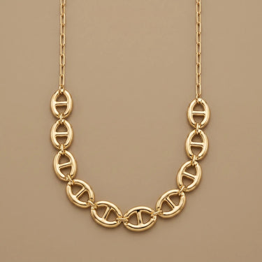 Polished gold statement chain necklace with oval link design, chunky luxury silhouette, and warm neutral backdrop.
