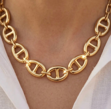 close-up of chunky gold oval link necklace on skin with glossy polished finish, warm lighting, and elevated luxury jewelry campaign styling.