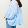 Woman wearing a light blue checkered blouse with ruffled sleeves on a plain background