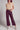 Front view of chocolate brown faux leather wide leg pants styled with beige top and sneakers, modern streetwear look