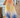 Merlot Pants, flowy resort pants with peach to yellow to ocean blue gradient worn on model walking on wooden dock near water showing lightweight fabric and wide-leg movement