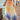Merlot Pants, flowy resort pants with peach to yellow to ocean blue gradient worn on model walking on wooden dock near water showing lightweight fabric and wide-leg movement