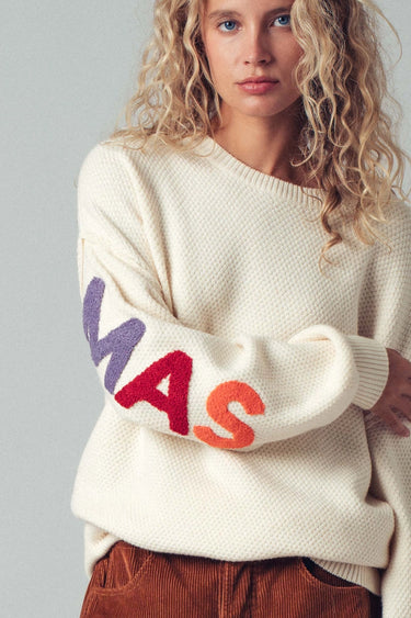 Person wearing a cream sweater with colorful letters on a plain background