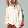 Woman wearing a white sweater with colorful letter sleeves against a gray background