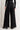 Back view of Midnight Lace Pants in black lace with satin waistband and wide-leg cut, styled with heeled boots.