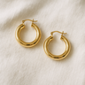 Mindy Huggie Earrings in gold displayed on a soft beige fabric background.