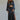 A woman wearing a long-sleeve crop satin top in black, paired with a high-waisted skirt with a side slit. 