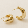 Gold plated sculptural hoop earrings with curved shape on white background.
